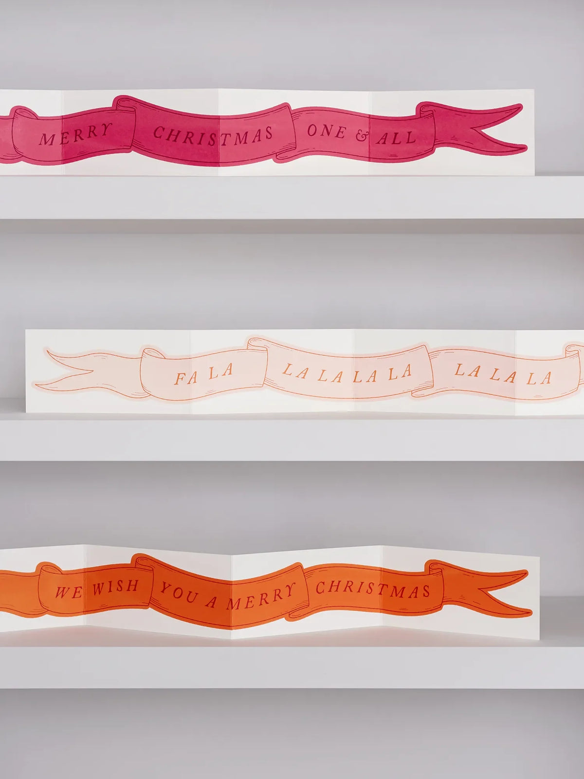 Cranberry Red, Marzipan Pink, Satsuma Orange screen printed concertina greeting card with ‘Merry Christmas One and All ’ 'Fa La La La' and 'We Wish You A Merry Christmas' in a banner across in a folk art style illustration, on three light blue shelves