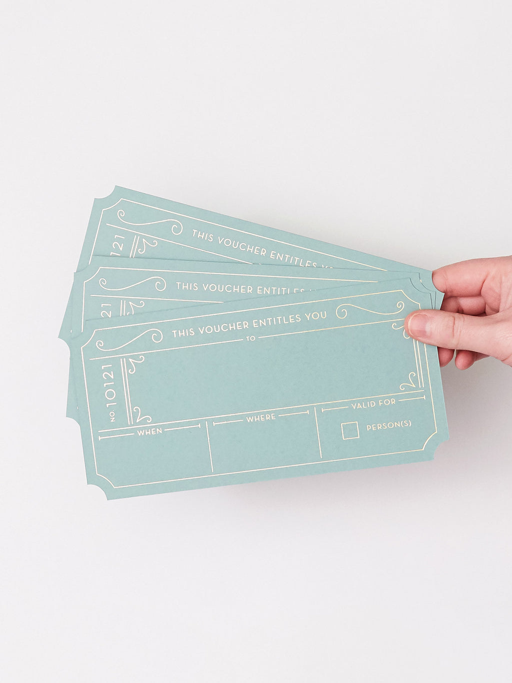 A hand holding three Golden Ticket vouchers in a Avocado Green with Hot Foiled Gold Text, set against a plain white background.
