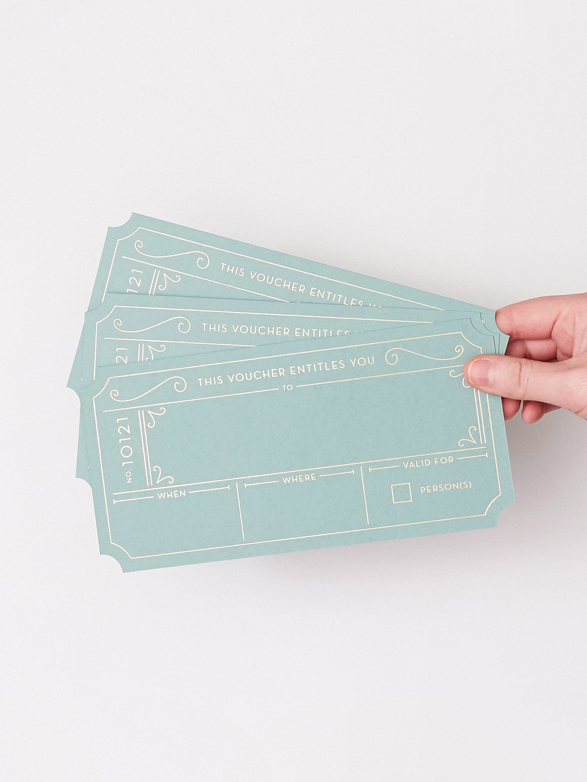 A hand holding three Golden Ticket vouchers in a Avocado Green with Hot Foiled Gold Text, set against a plain white background.