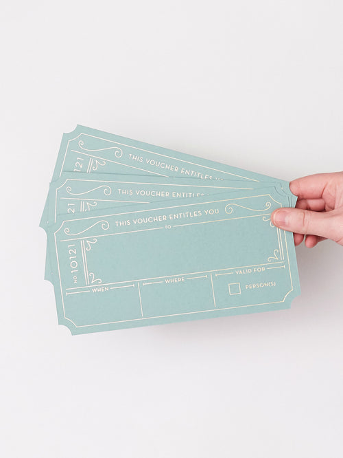 A hand holding three Golden Ticket vouchers in a Avocado Green with Hot Foiled Gold Text, set against a plain white background.