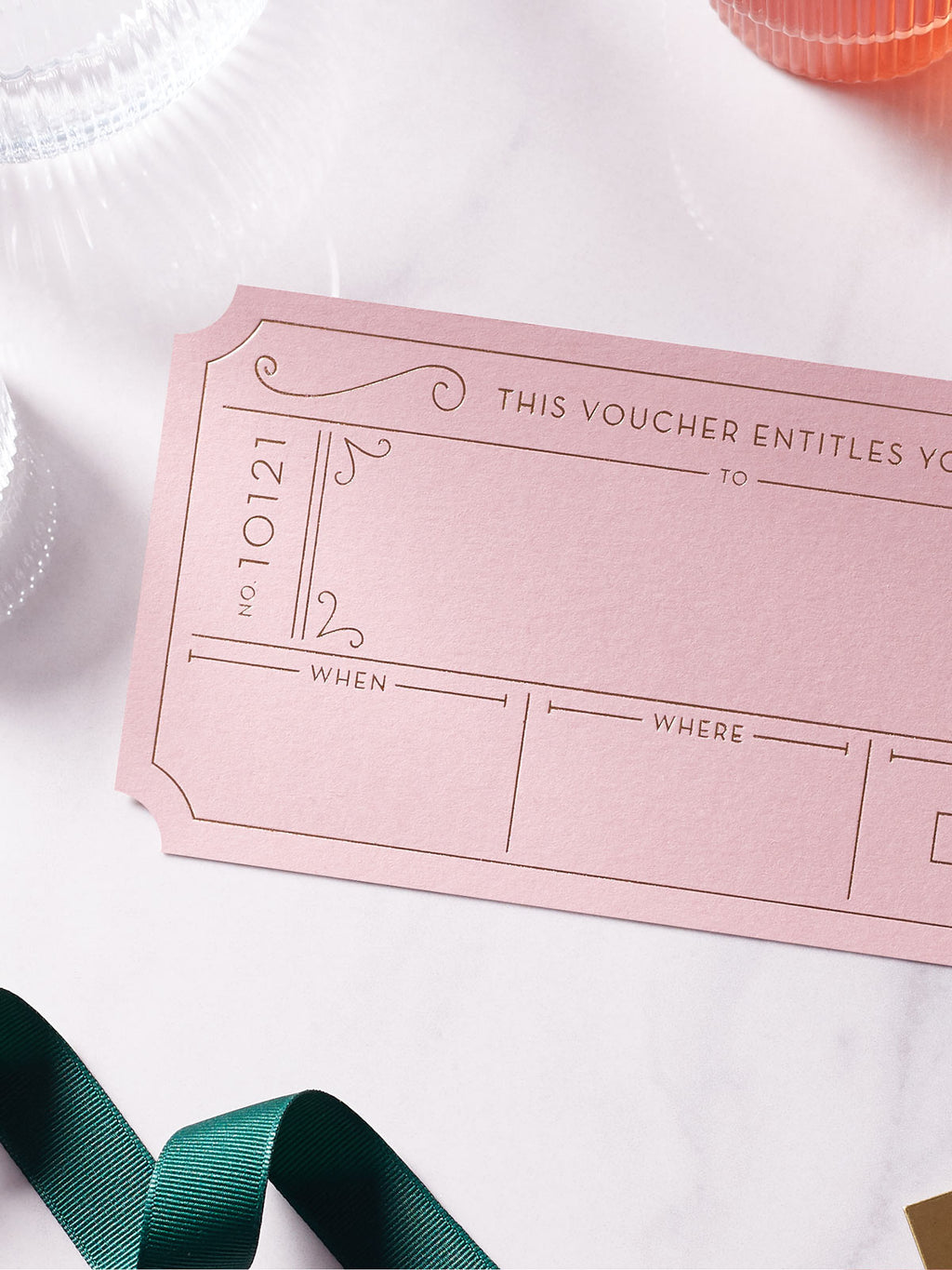 Dusty Pink Golden Ticket voucher with Hot Foiled in gold , green ribbon around it on a white background