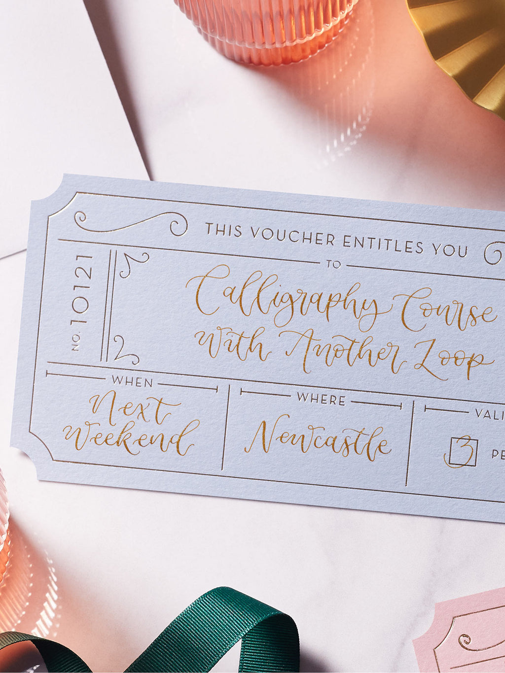 blue event ticket with gold foil on a marble tabletop, personalised with modern calligraphy to create a bespoke golden ticket