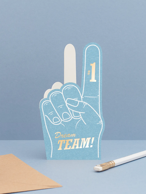 Hot foiled die-cut foam finger valentines card featuring ‘dream team’ in gold foil on a blue foam finger, displayed on a blue background.