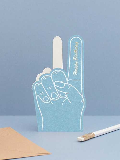 Hot foiled die-cut foam finger birthday card featuring ‘happy birthday’ in gold foil on a blue foam finger, displayed on a blue background.
