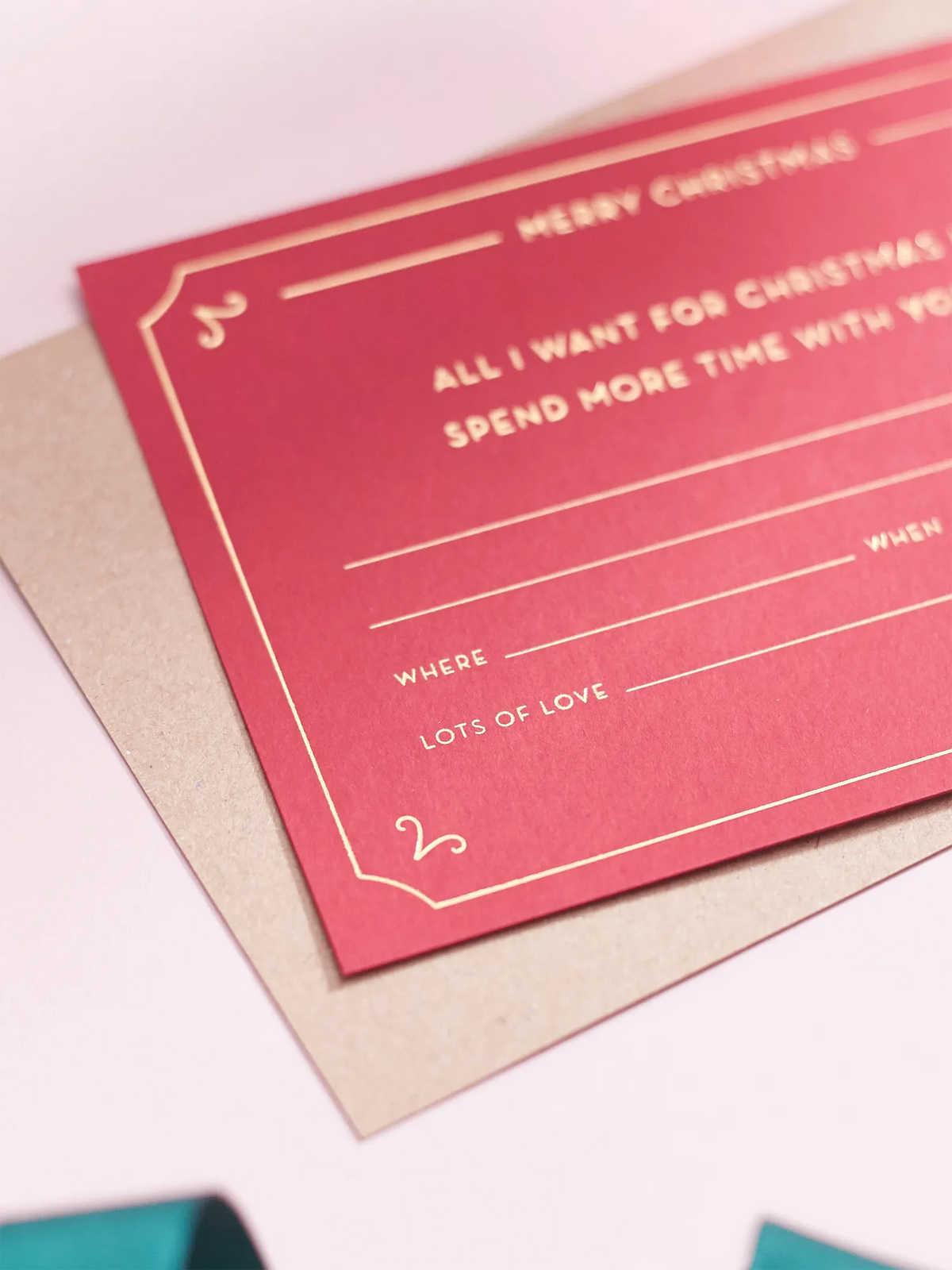 A red christmas Gift Of Time Voucher with gold foil lettering, placed on top of a brown kraft envelope.