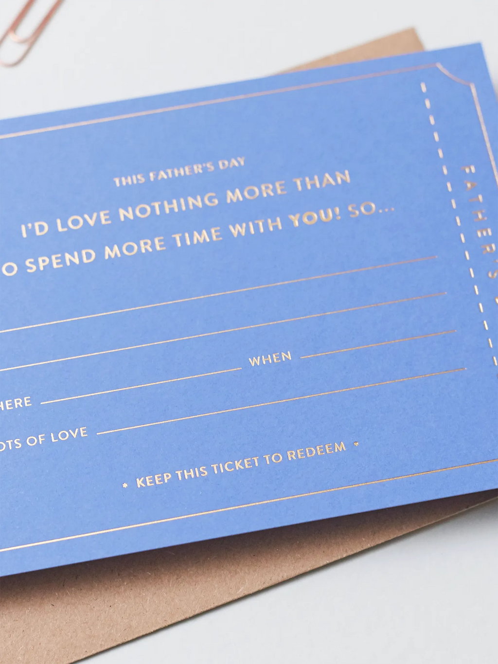 A blue Father's Day Gift Of Time Voucher with gold foil lettering, placed on top of a brown kraft envelope, close up