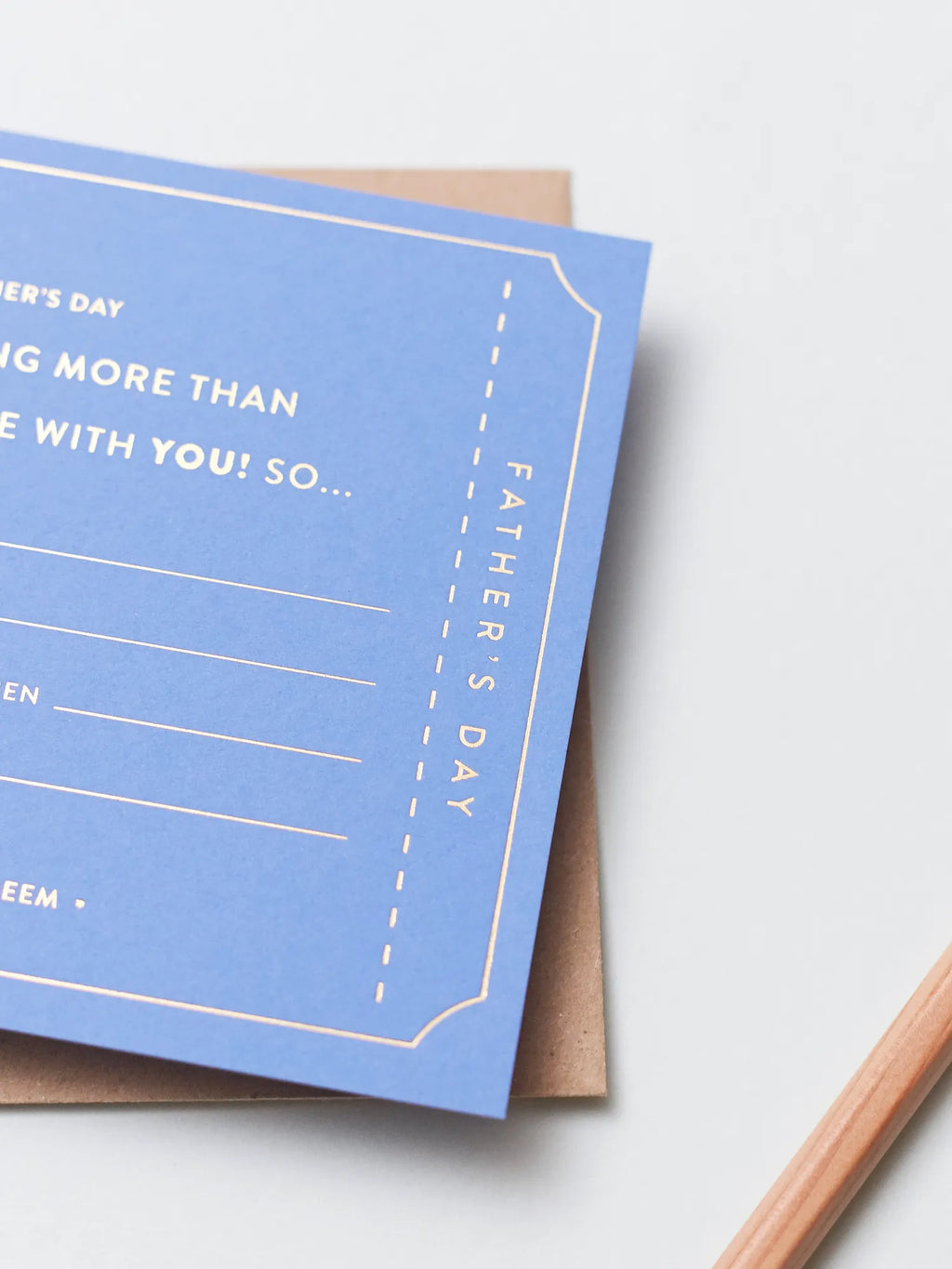 A blue Father's Day Gift Of Time Voucher with gold foil lettering, placed on top of a brown kraft envelope on a white surface.