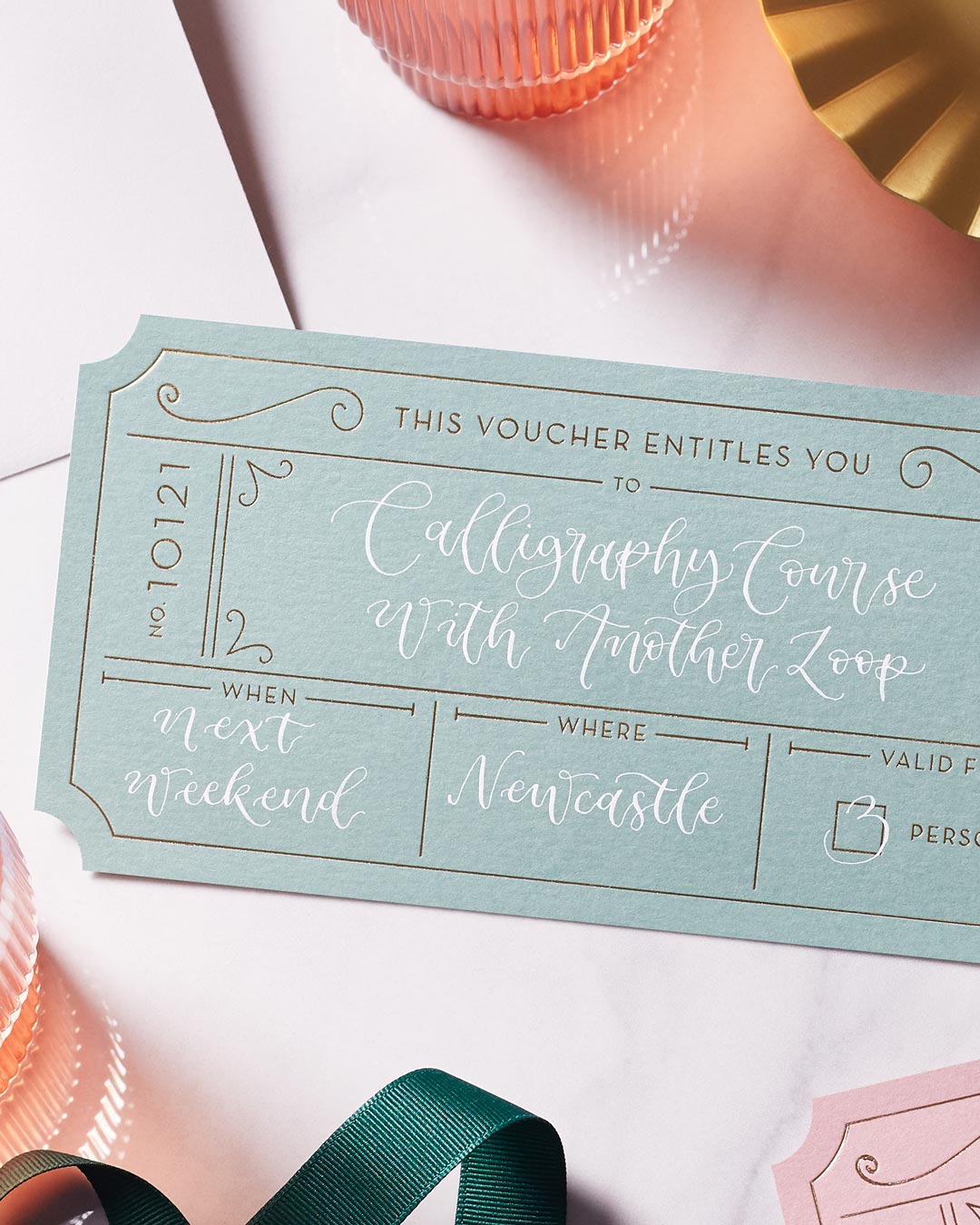 green event ticket with gold foil on a marble tabletop, personalised with modern calligraphy in white ink to create a bespoke golden ticket