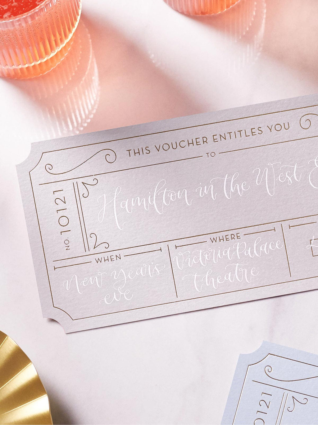 grey event ticket with gold foil on a marble tabletop, personalised with modern calligraphy to create a bespoke golden ticket