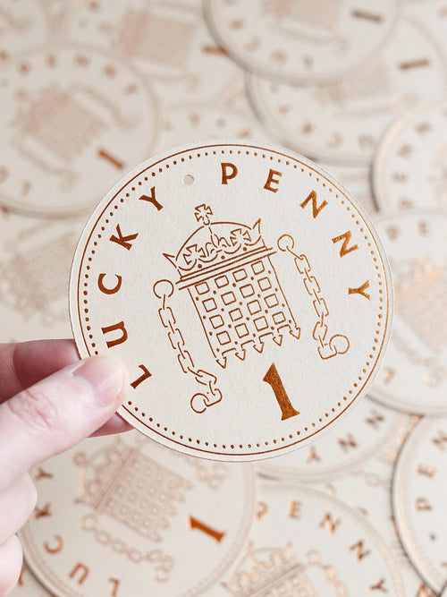 A hand holds a round, lucky penny token with more tokens in the background