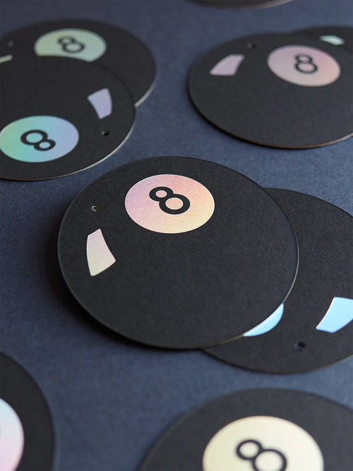 A close-up of several round black vouchers featuring an 8-ball design with a holographic design arranged on a dark blue surface.