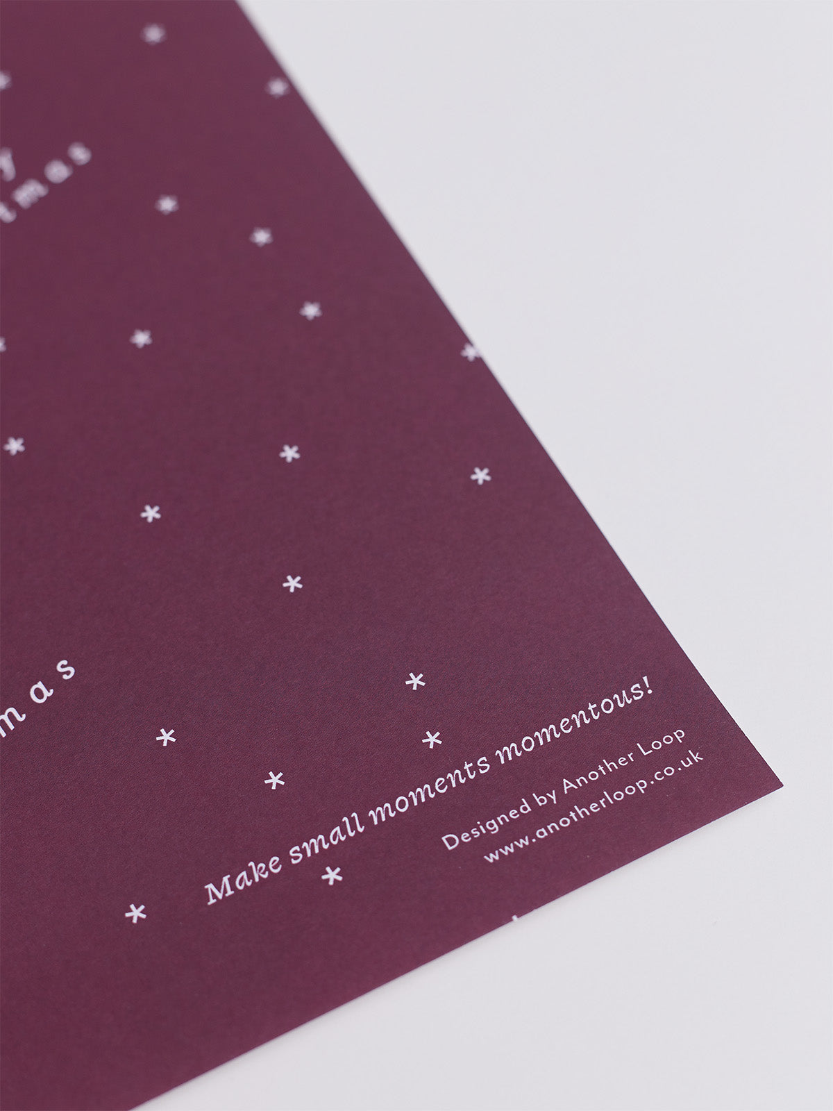 A close-up of a an Burgundy wrapping paper printed with small white stars and white text, including the phrase 'Make small moments momentous!' and 'Designed by Another Loop'.