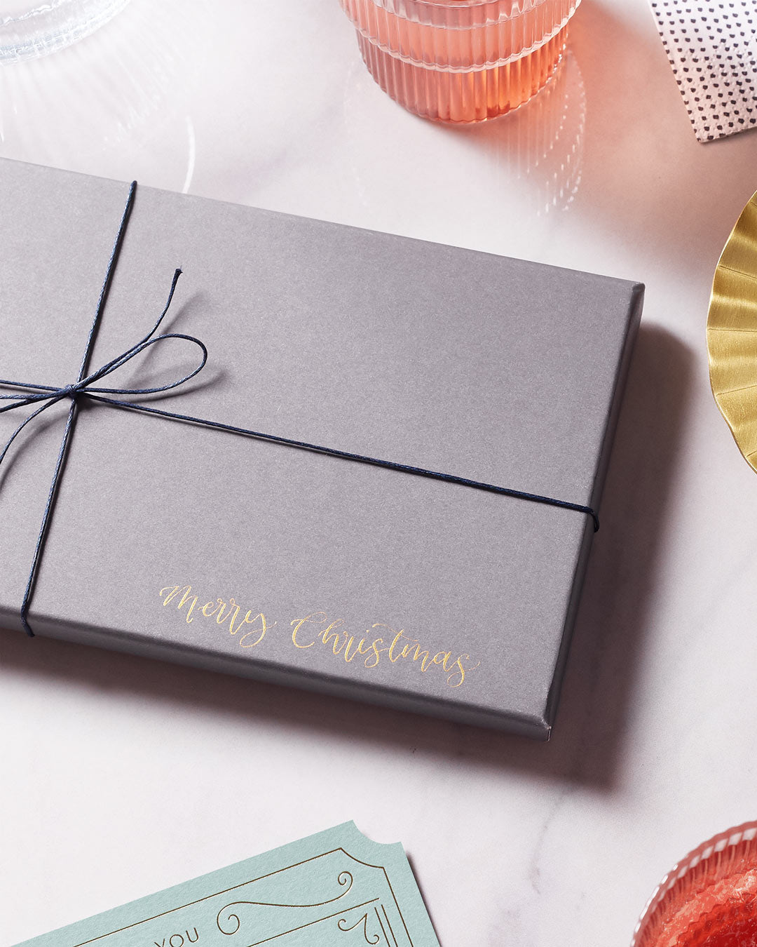 grey gift box on a marble tabletop with 'Merry Christmas' written in gold ink in the corner